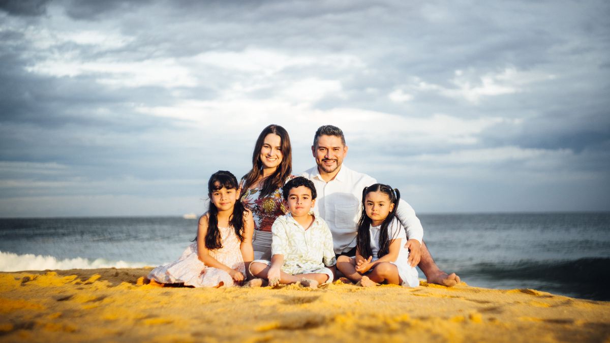 Michelle y Efrén Ruiz con sus tres hijos, sentados en la arena al atardecer.
