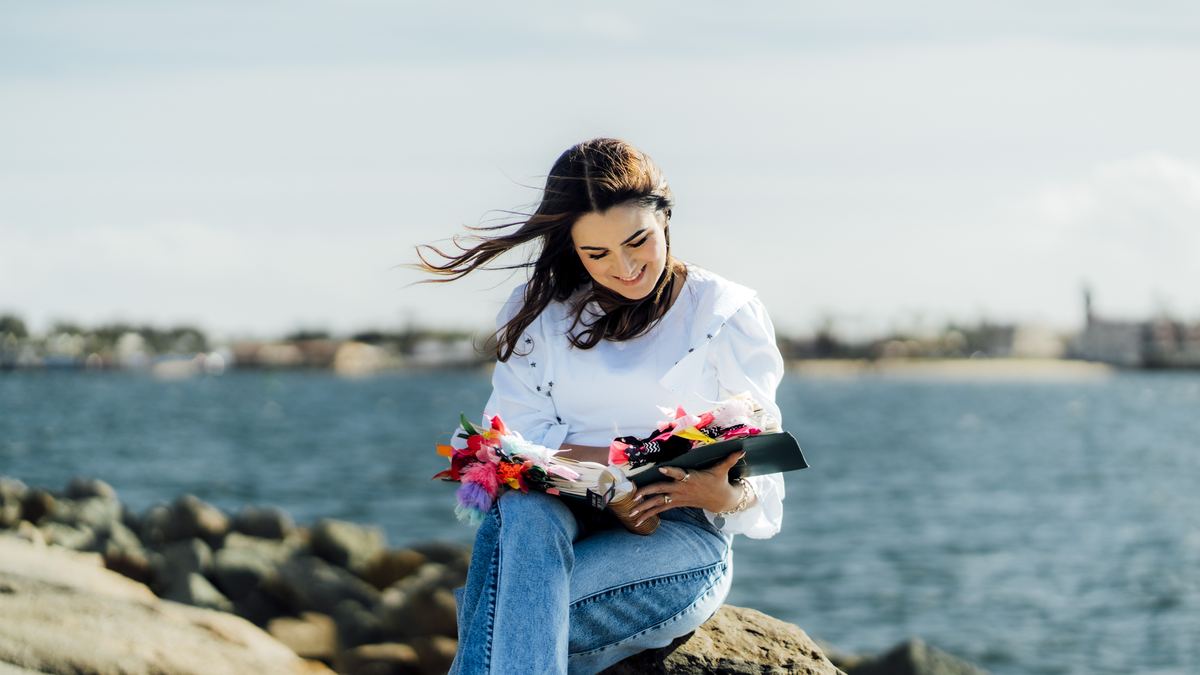 Michelle Ruiz sentada frente a la bahía con su Biblia abierta sobre las piernas, el cabello movido por el viento.