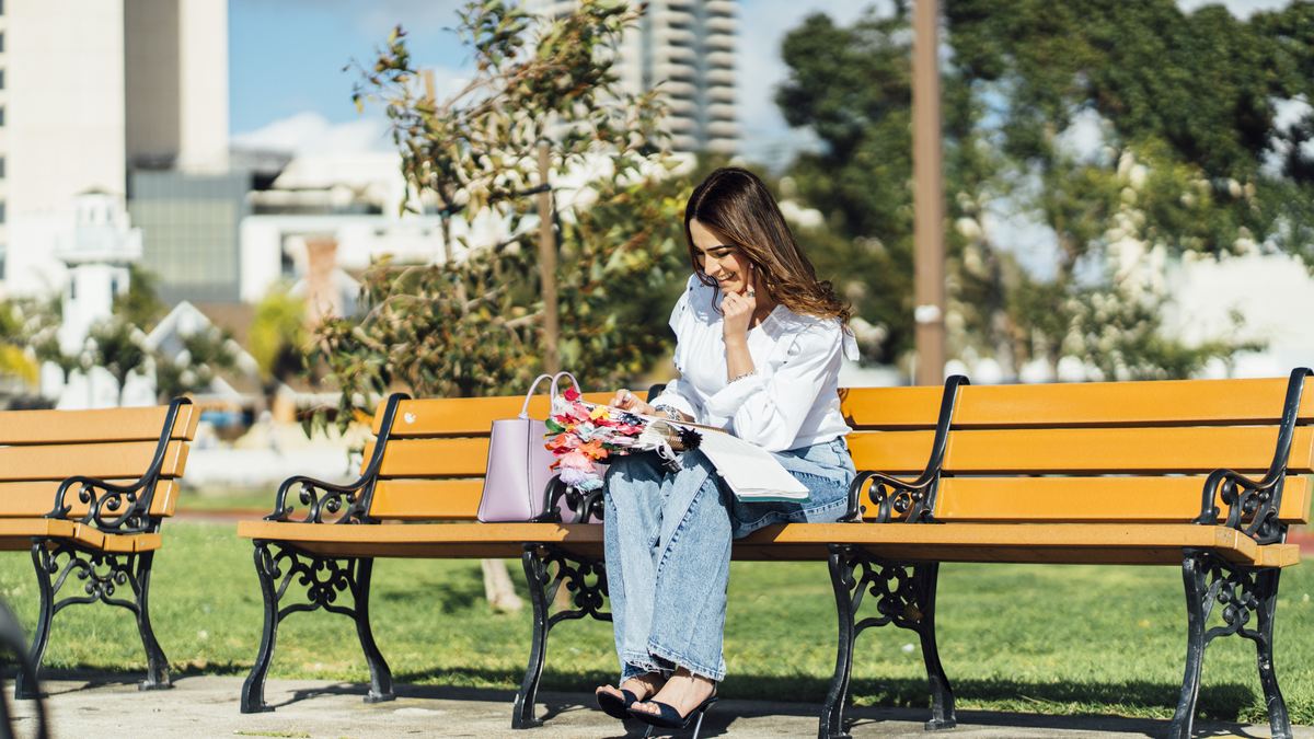 Michelle Ruiz sentada en una banca del parque, escribiendo en su libreta.