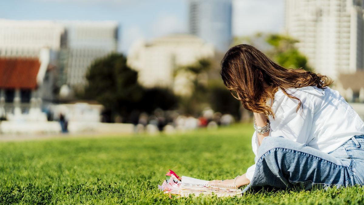 Michelle Ruiz inclinada sobre el pasto, escribiendo en su Biblia abierta.